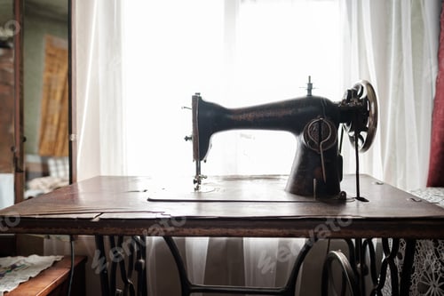 Preview: Vintage mechanical sewing machine with a table stands by a window in a rustic house