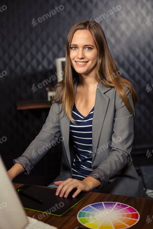 Preview: Woman graphic designer wearing business casual using laptop and drawing on tablet at studio desk
