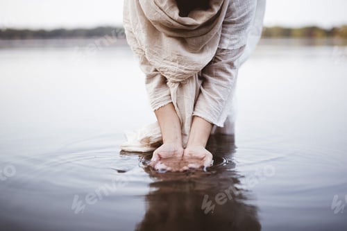 Preview: Closeup shot of a female wearing a biblical robe standing in the water while washing her hands