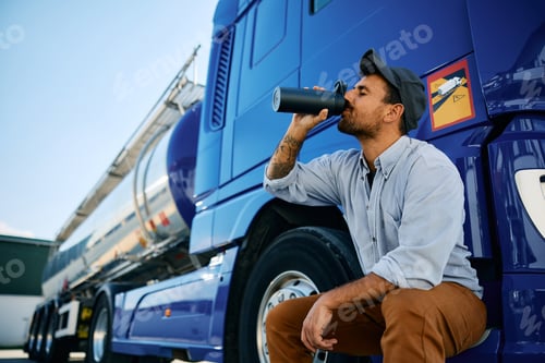 Preview: Truck driver drinking water from a bottle on a parking lot.