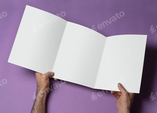 Preview: Hand holding an opened trifold catalog with blank pages on purple background
