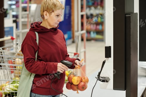 Preview: Blond mature female consumer in casualwear looking at screen with price