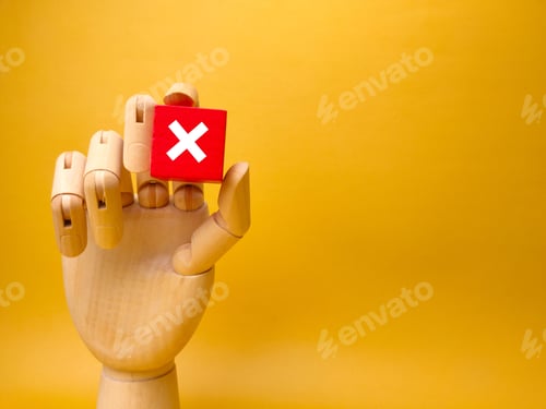 Preview: Wooden hand holding a block with the X symbol on it on a yellow background with a copy space