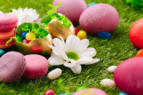 Preview: Close up photo of colored Easter eggs and candies on grass