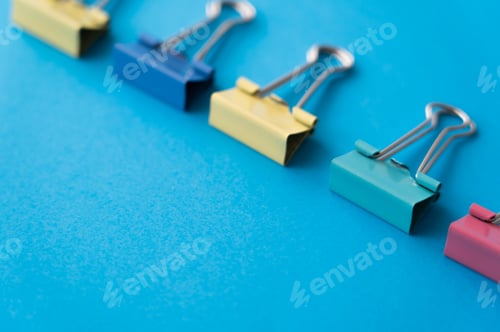 Preview: flat lay of colorful pastel fold back clips on blue