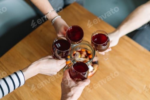 Preview: Group of people toasting with glasses of red wine over a wooden table with a pitcher of sangria