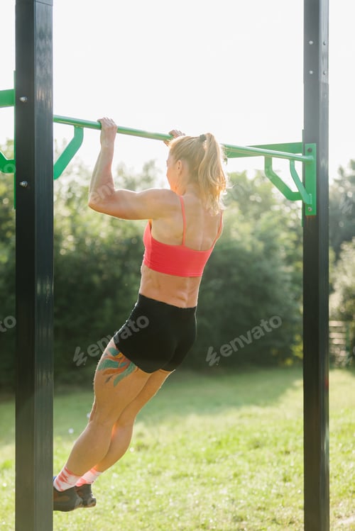 Preview: Woman exercising outdoors doing chin-ups on pull-up bar