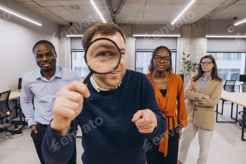 Preview: Businessman holding magnifying glass pointing with his finger leading his multi ethnic team