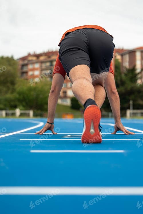 Preview: vertical Runner Crouched at Starting Line Ready to Begin Race on Blue Athletic Track