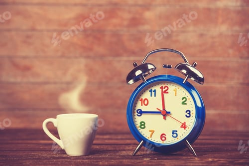 Preview: Cup of coffee and alarm clock on wooden table.