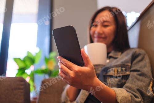 Preview: Blurred image of a young woman holding and using mobile phone while drinking in cafe