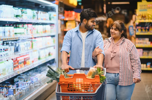 Preview: Indian couple choosing food, pushing shopping cart in supermarket