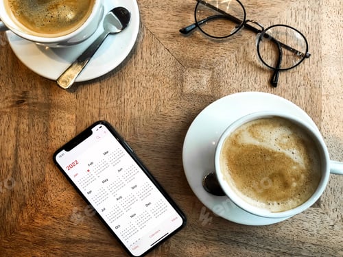 Preview: Calendar flat lay: couple is making plans for new year in a cafe. Smartphone cups of coffee on table