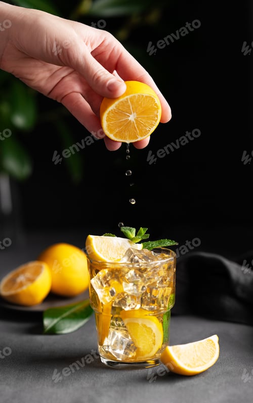 Preview: A hand squeezes juice from a lemon into a glass with lemonade with ice and mint