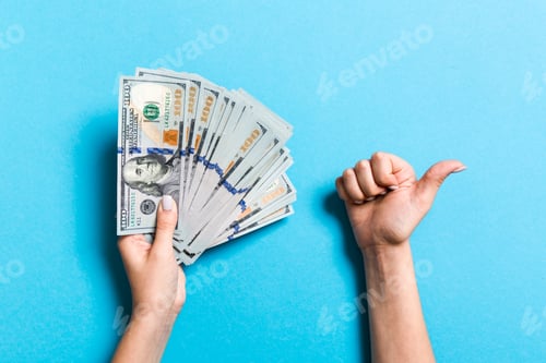 Preview: Top view of one hundred dollar bills in one hand and showing thumb up