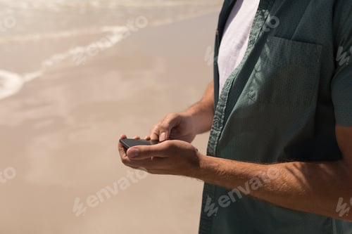 Preview: Mid section of young man using mobile phone on beach in the sunshine
