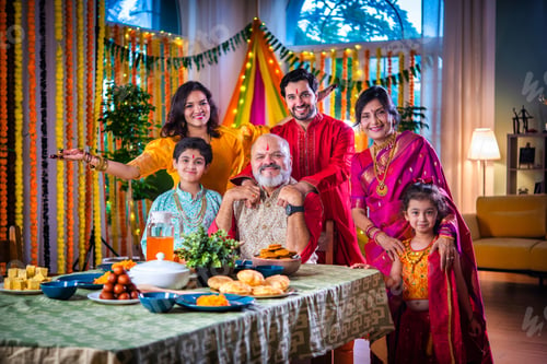 Preview: Portrait of happy Indian family in traditional outfit celebrating Diwali at home eating food