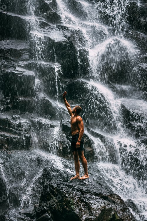 Preview: Back view of a man standing by waterfalls with arms outstretched