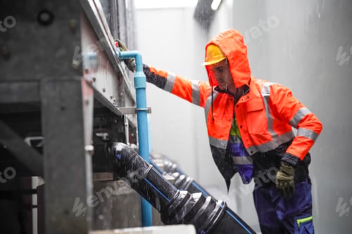 Preview: Worker in safety gear inspecting drainage system during rainy weather
