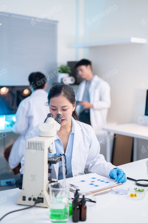 Preview: Woman scientist researcher using microscope looking at test sample and working with colleague in lab