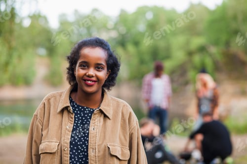 Preview: Portrait of happy woman standing at lakeshore with friends in background