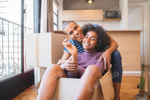 Preview: Latin couple having fun with cardboard boxes in new house.