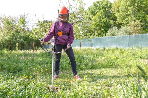 Preview: Woman farmer mows the grass in the backyard using string trimmer