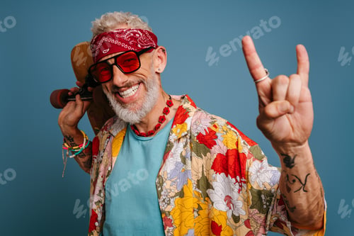 Preview: Hipster mature man in stylish funky shirt carrying longboard and gesturing against blue background