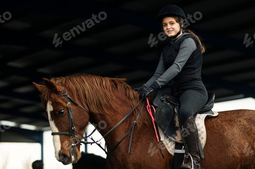 Preview: Young girl in helmet and special clothes riding a horse on the sandy ground of the paddock
