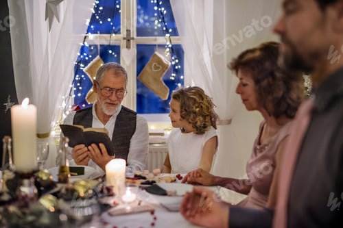 Preview: Senior man with extended family indoors celebrating Christmas, reading Bible.