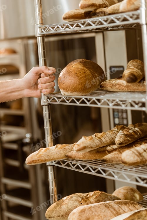 Preview: baker holding shelves with fresh loaves of bread on baking manufacture