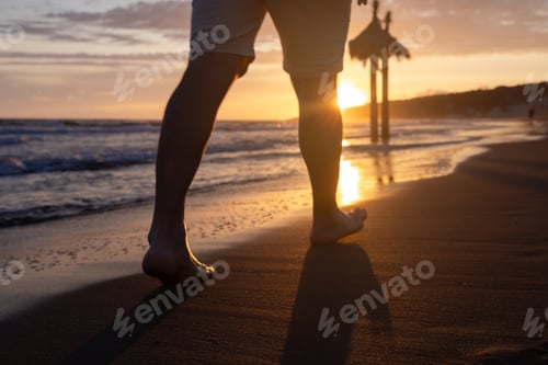 Preview: The legs of a man walking barefoot on a sandy beach. A sunny path