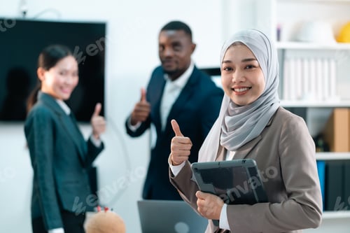 Preview: Confident Muslim businesswoman smiling and giving thumbs up while holding a tablet