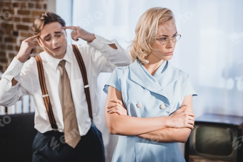 Preview: offended woman standing with crossed arms and looking away while emotional husband gesturing with