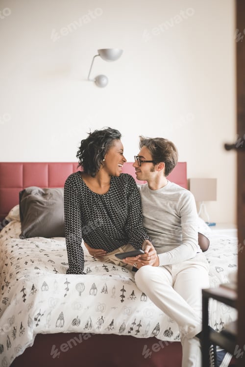 Preview: Young handsome mixed race couple in their house sitting on their bed