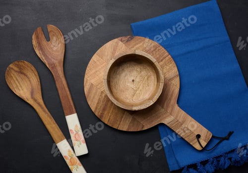 Preview: Empty bowl and wooden spoons on a black table, top view