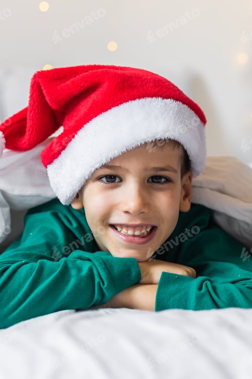 Preview: Child boy in green xmas pajamas holds a Christmas gift in his hands while sitting in bed. Generation