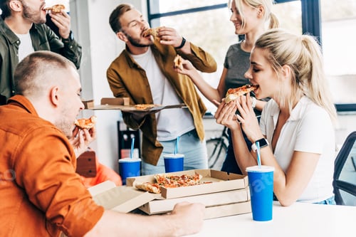 Preview: group of happy young entrepreneurs eating pizza for lunch together while working on startup at