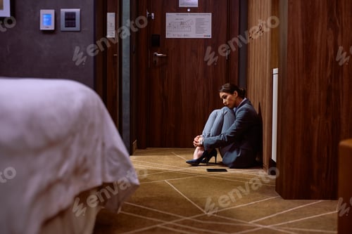Preview: Sad businesswoman sitting on the floor in a hotel room.