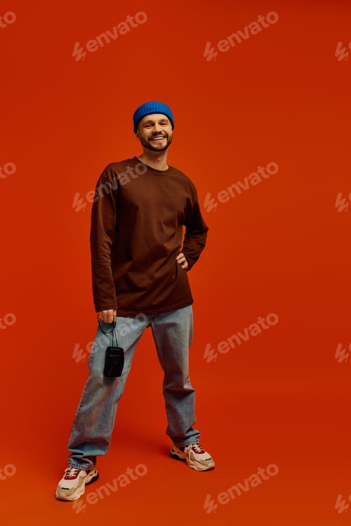 Preview: Young man in casual outfit poses confidently against a vibrant orange backdrop