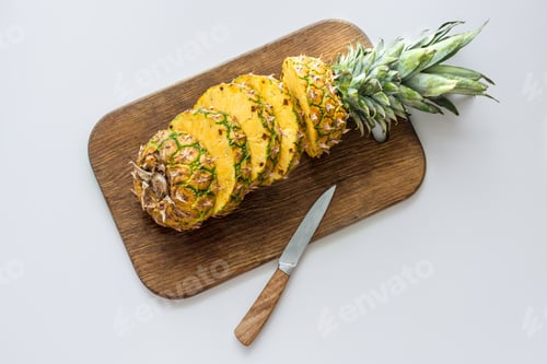 Preview: top view of fresh sliced pineapple on wooden cutting board with knife, isolated on white