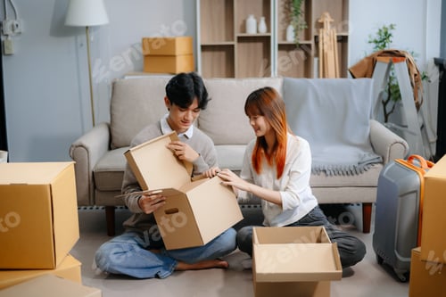 Preview: Young couple preparing for a move, packing boxes and a suitcase in a cozy living room. Perfect
