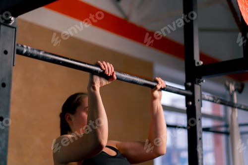 Preview: in the gym a coach girl in black leggings and a top is doing pull-ups on the horizontal bar