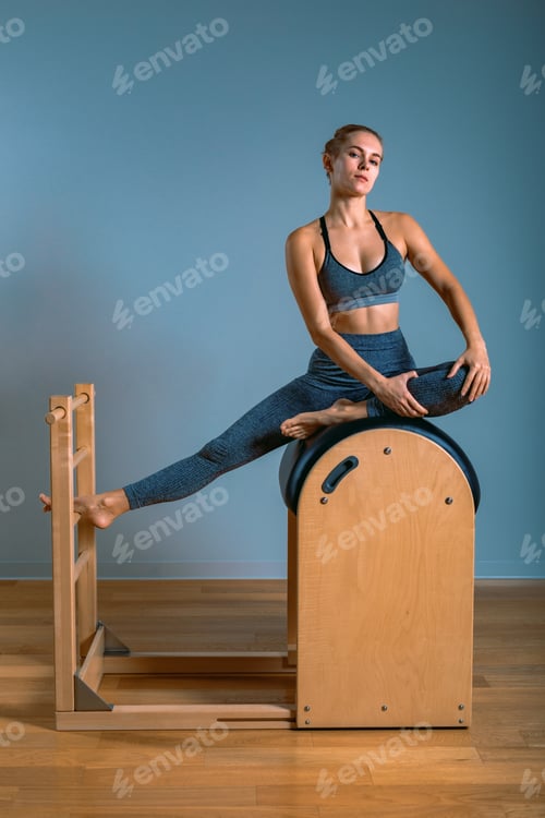 Preview: Beautiful positive blond woman is being prepared performing pilates exercise, training on barrel