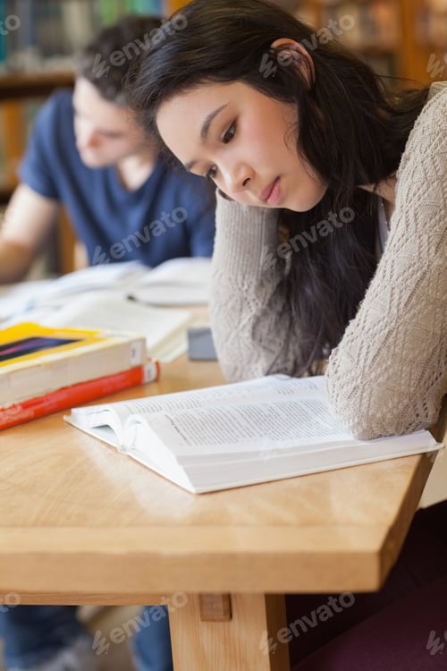 Preview: Student Sitting At A Table In A Library While Reading A Book And Being Concentrated