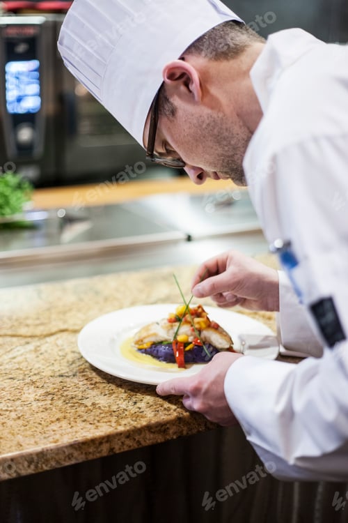 Preview: A caucasian male chef putting the finishing touches on a plate of fish in a commercial kitchen.