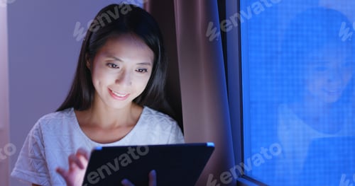 Preview: Woman looking at tablet computer in the evening