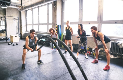 Preview: Group of young fit people cheering at man exercising with ropes in gym