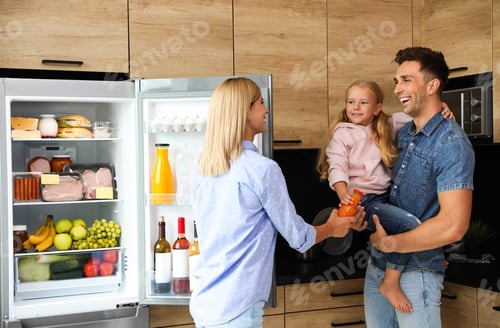 Preview: Happy family with bottle of juice near refrigerator in kitchen