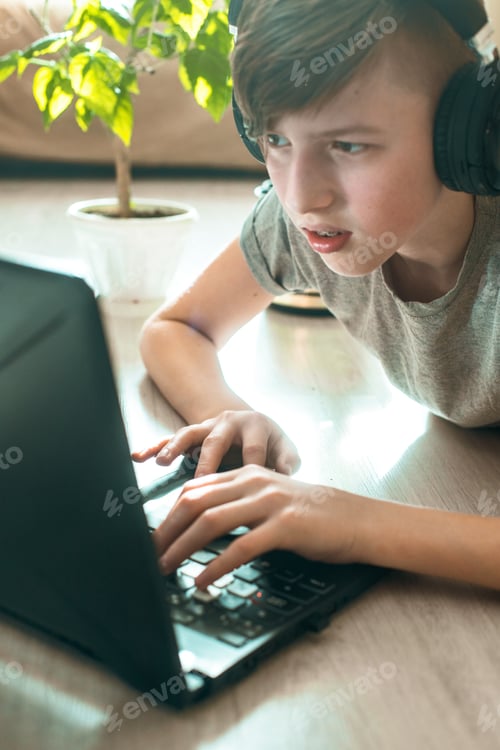 Preview: boy in wireless gamer headphones lies on floor near laptop